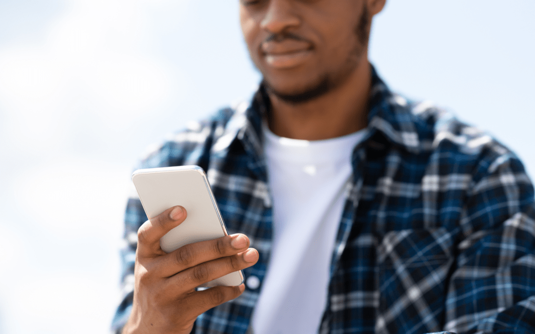 Junge Person in kariertem Hemd nutzt ein Smartphone, während sie sich im Freien auf einen hellen Tag konzentriert.